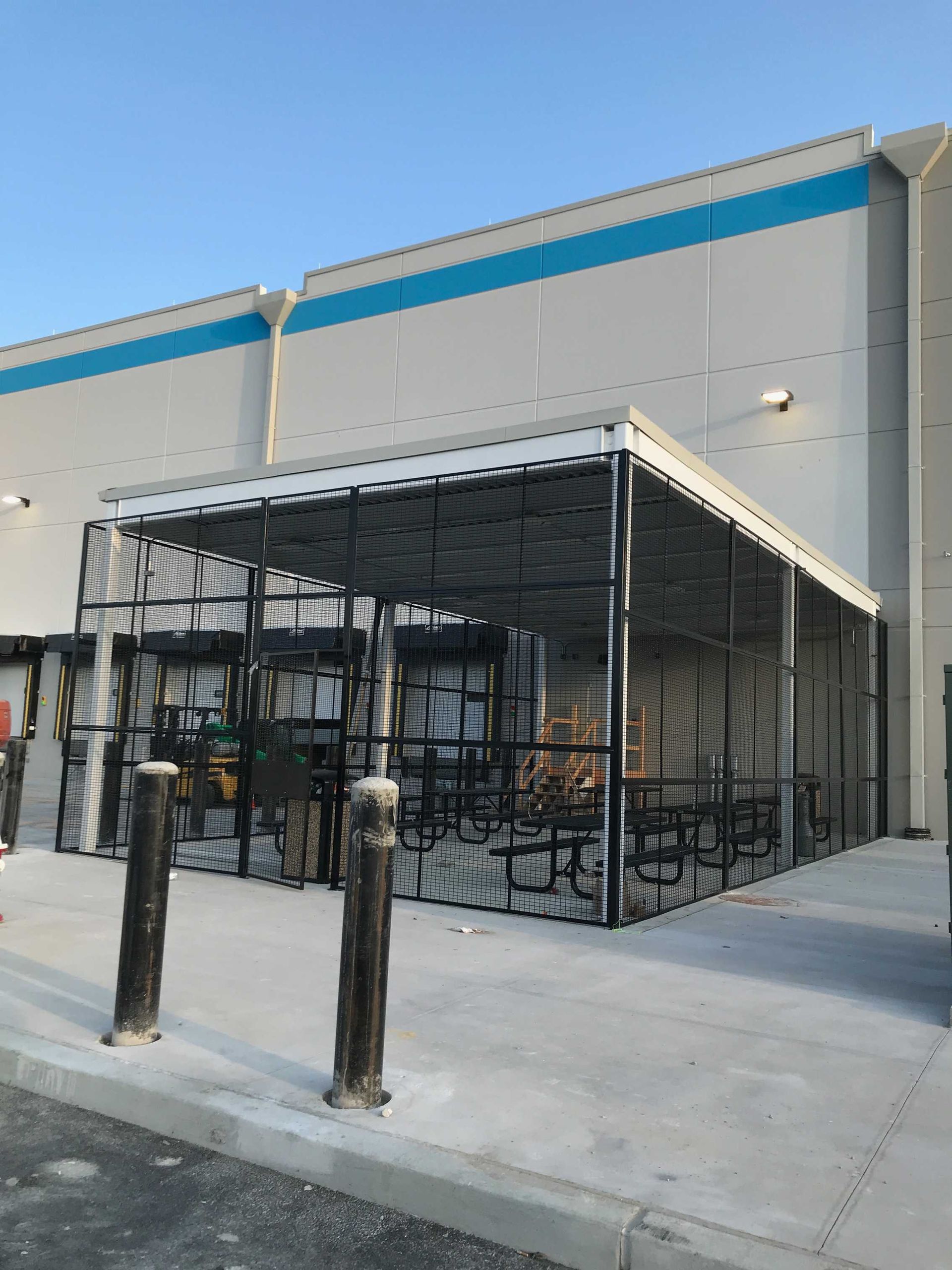 Covered outdoor break area at an Amazon warehouse with black metal fencing and picnic tables.