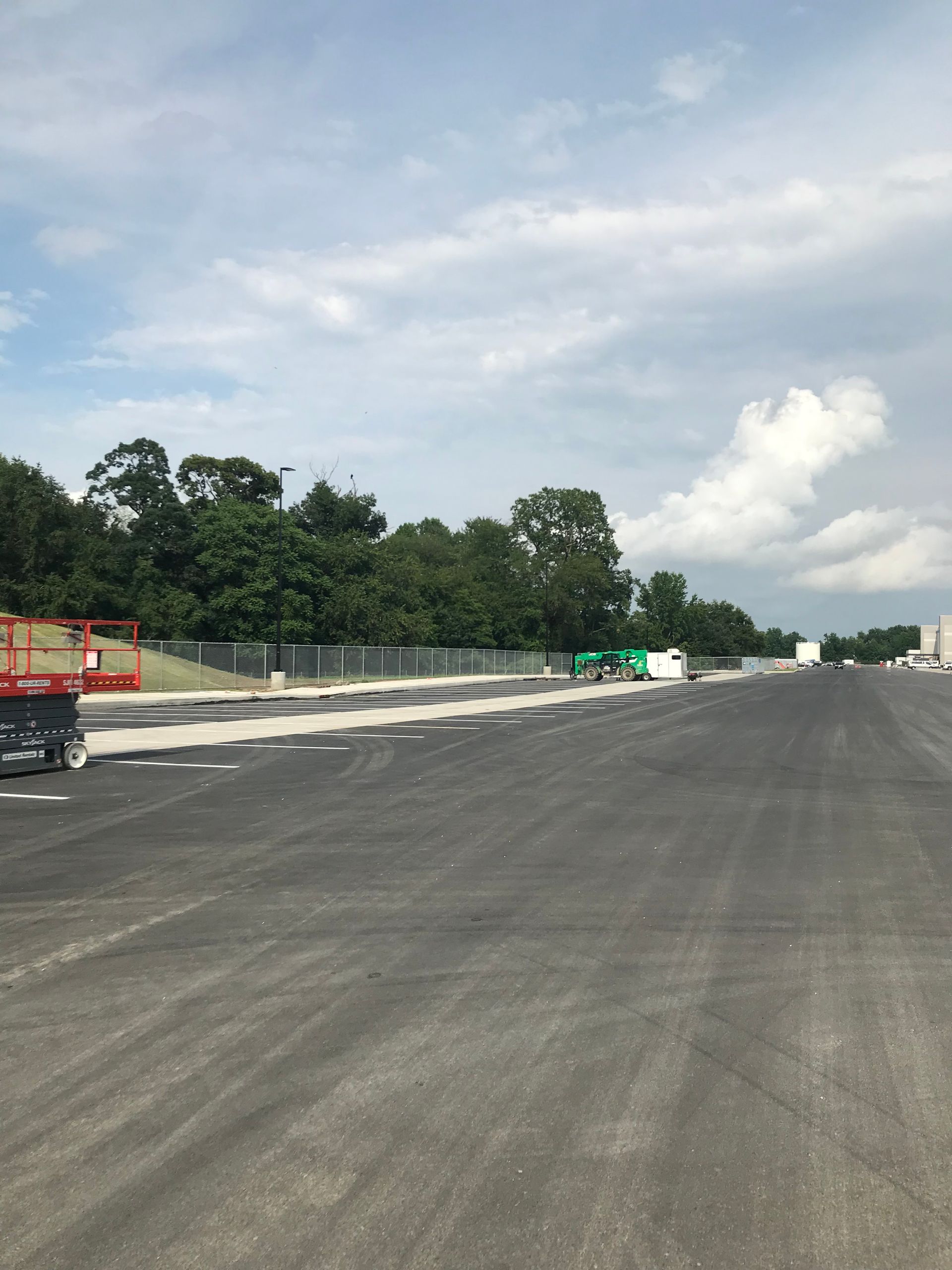 An asphalt parking lot with a cloudy sky and trees in the background.