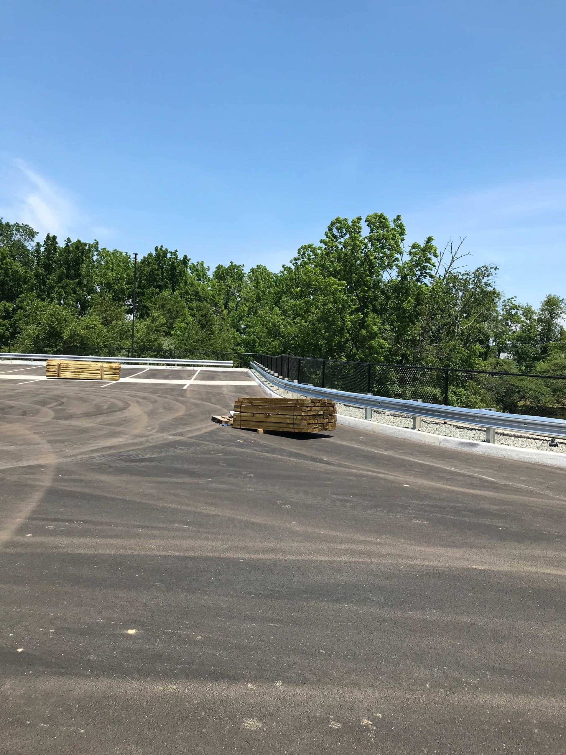 Rooftop with stacks of lumber, surrounded by trees under a blue sky.