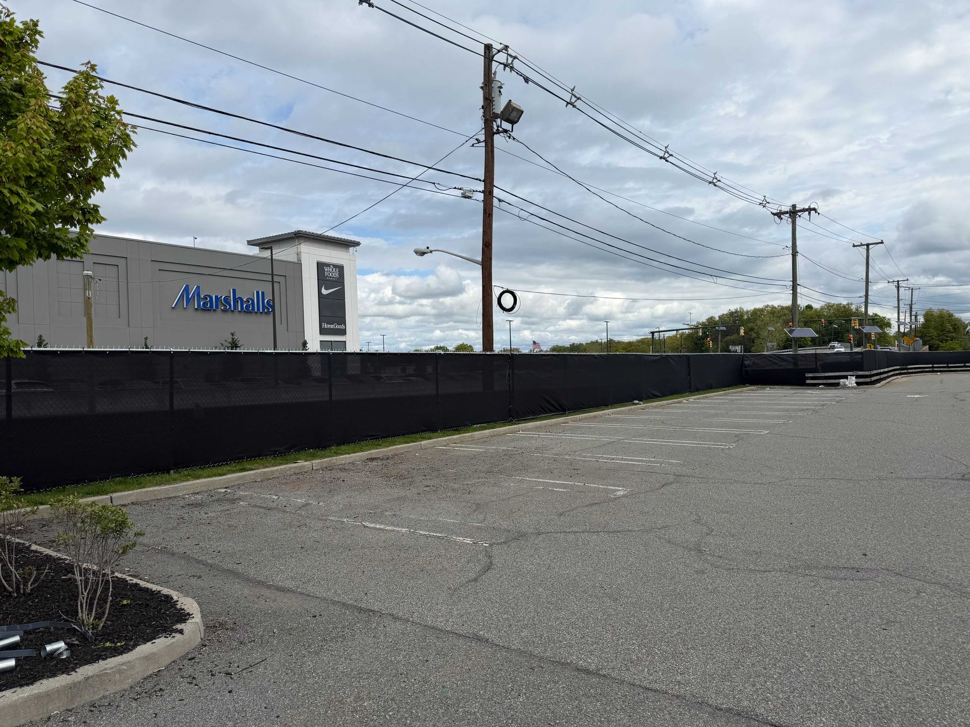 Parking lot beside a low building with a blue sign, black fence, utility poles, and cloudy sky