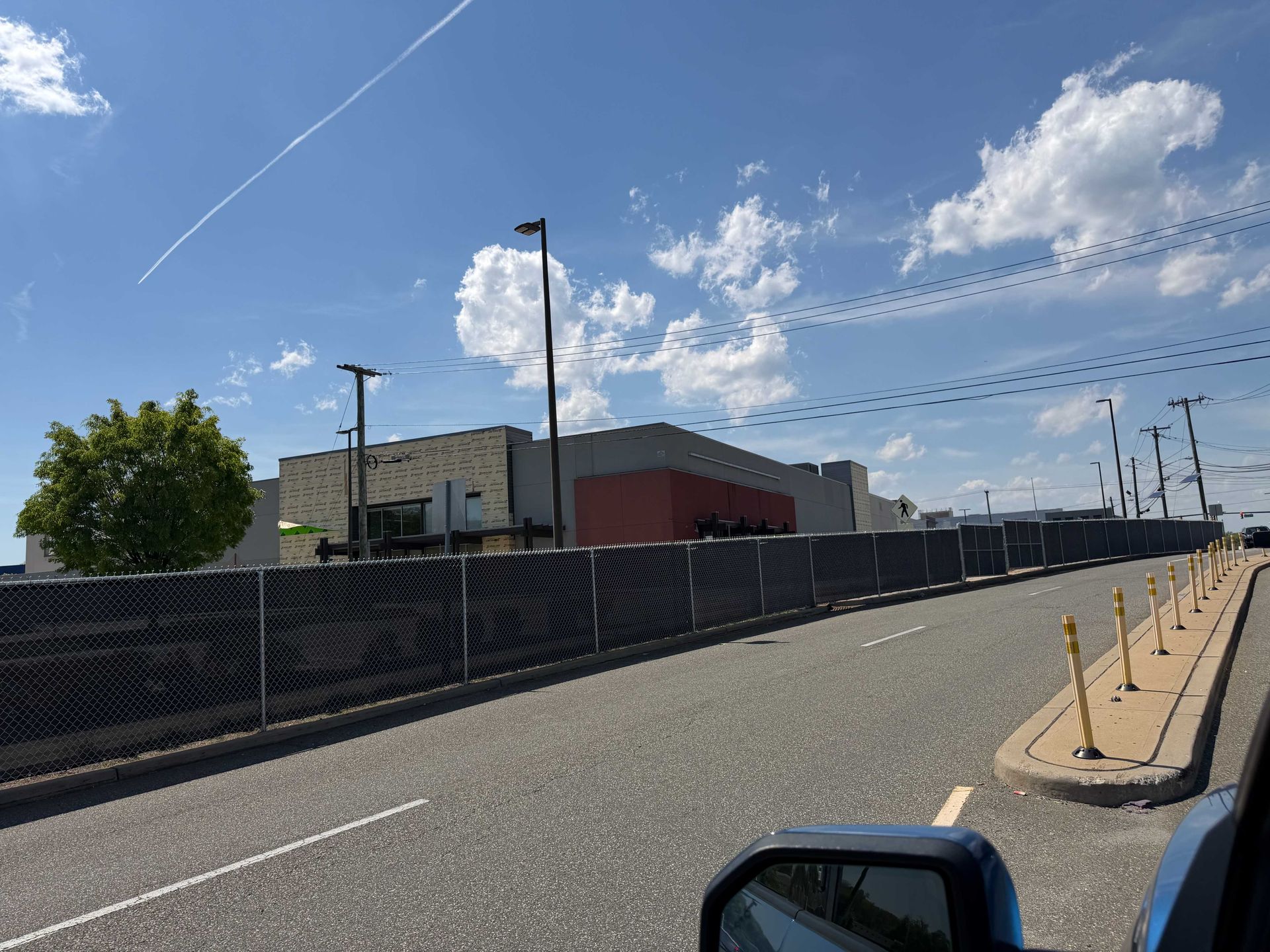 Empty parking lot beside a chain-link fence and low industrial buildings under a blue sky.