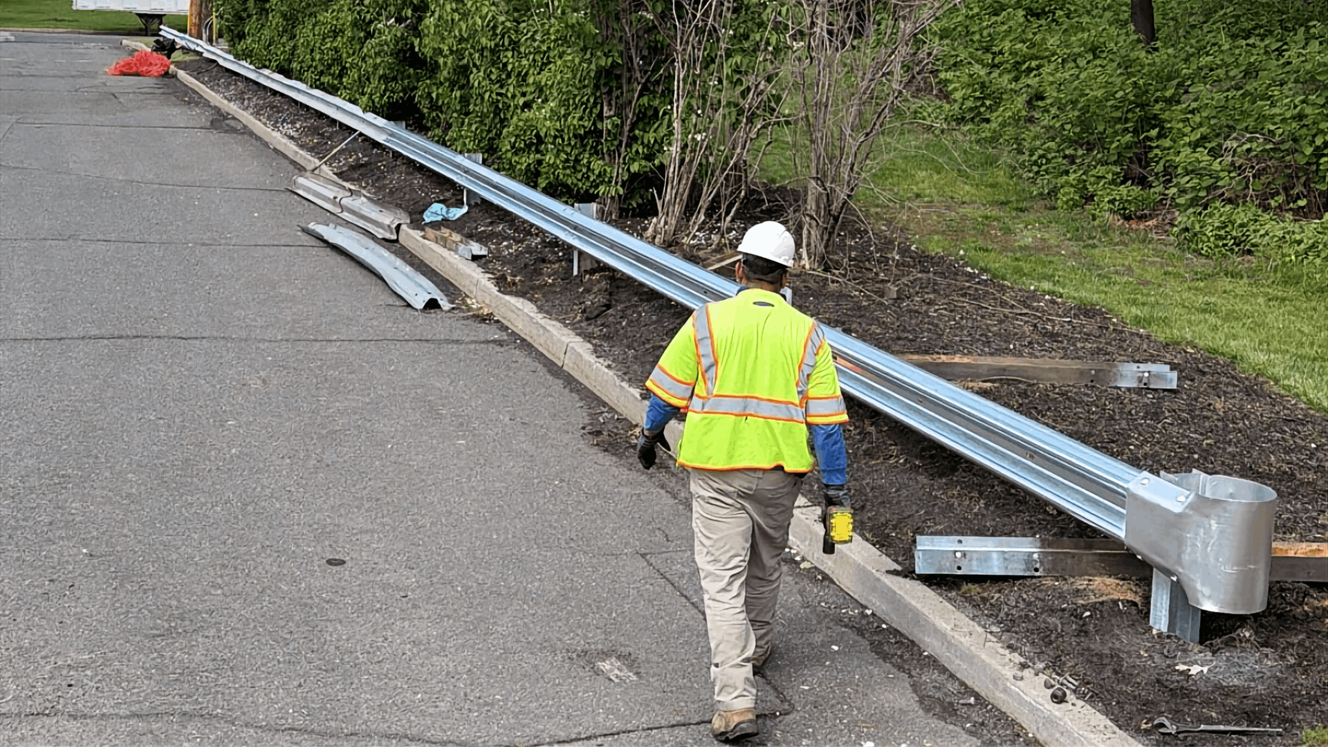 Worker in a hard hat inspecting a damaged highway guardrail beside a road edge
