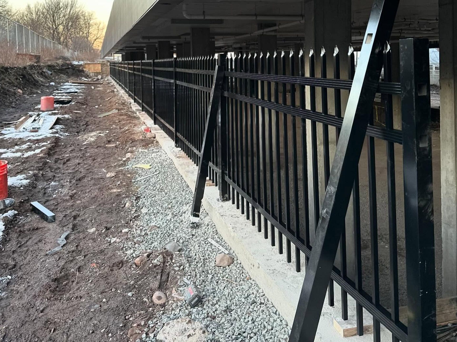 Black metal fence along a concrete structure, next to a muddy construction area.