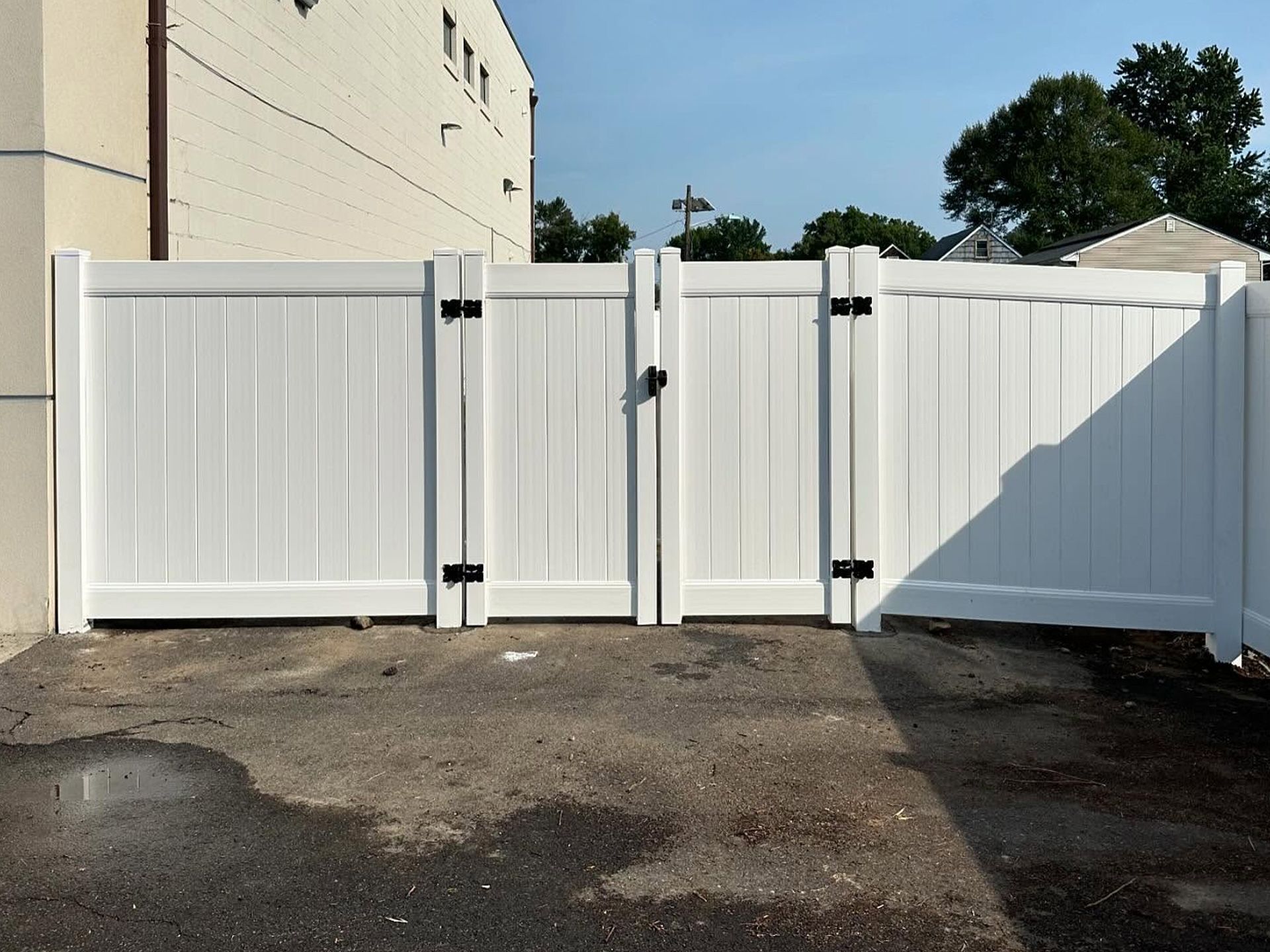 White vinyl double gate with black hardware, set in a paved area, next to a building.