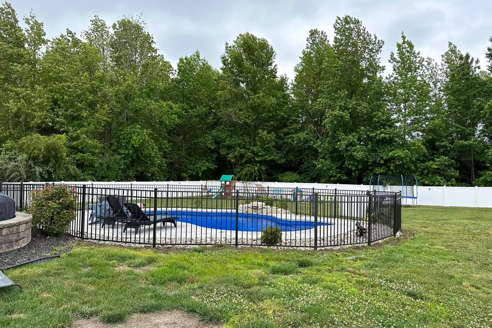 Pool enclosed by black fence and white fence with trees in the background.