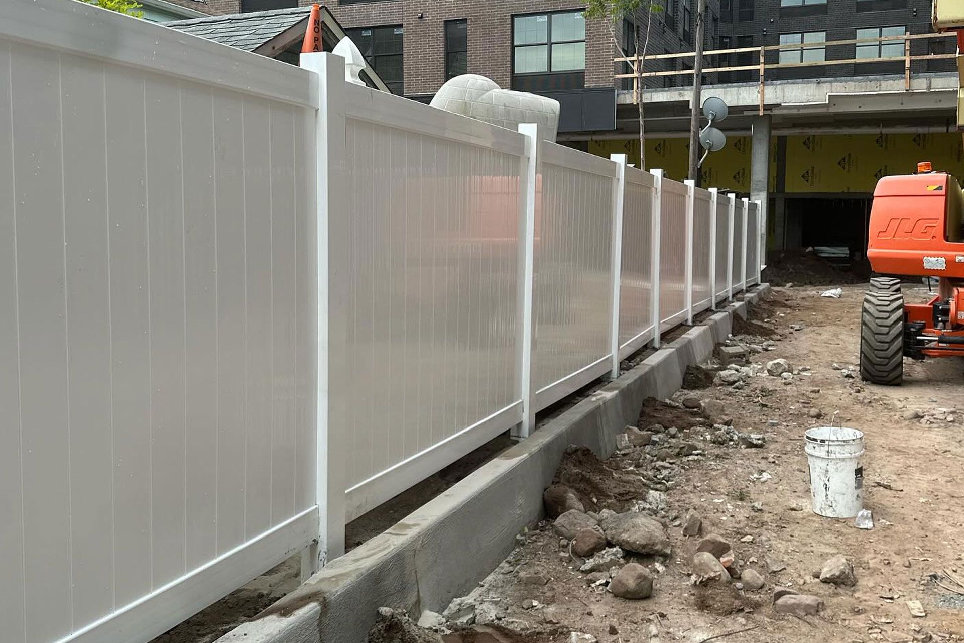 White vinyl fence at a construction site, near building and orange lift.