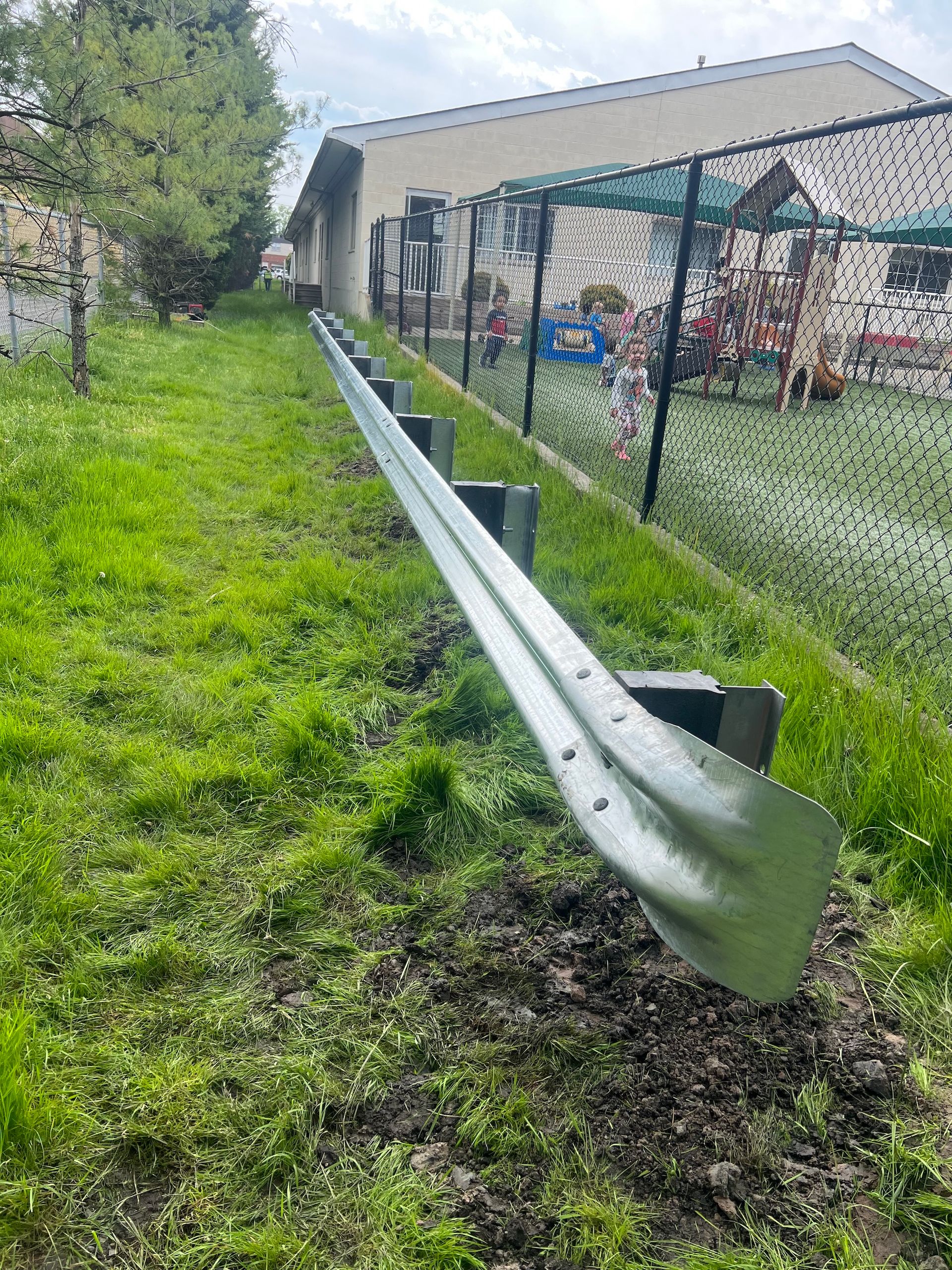 Guardrail on a grassy slope next to a building and fence.