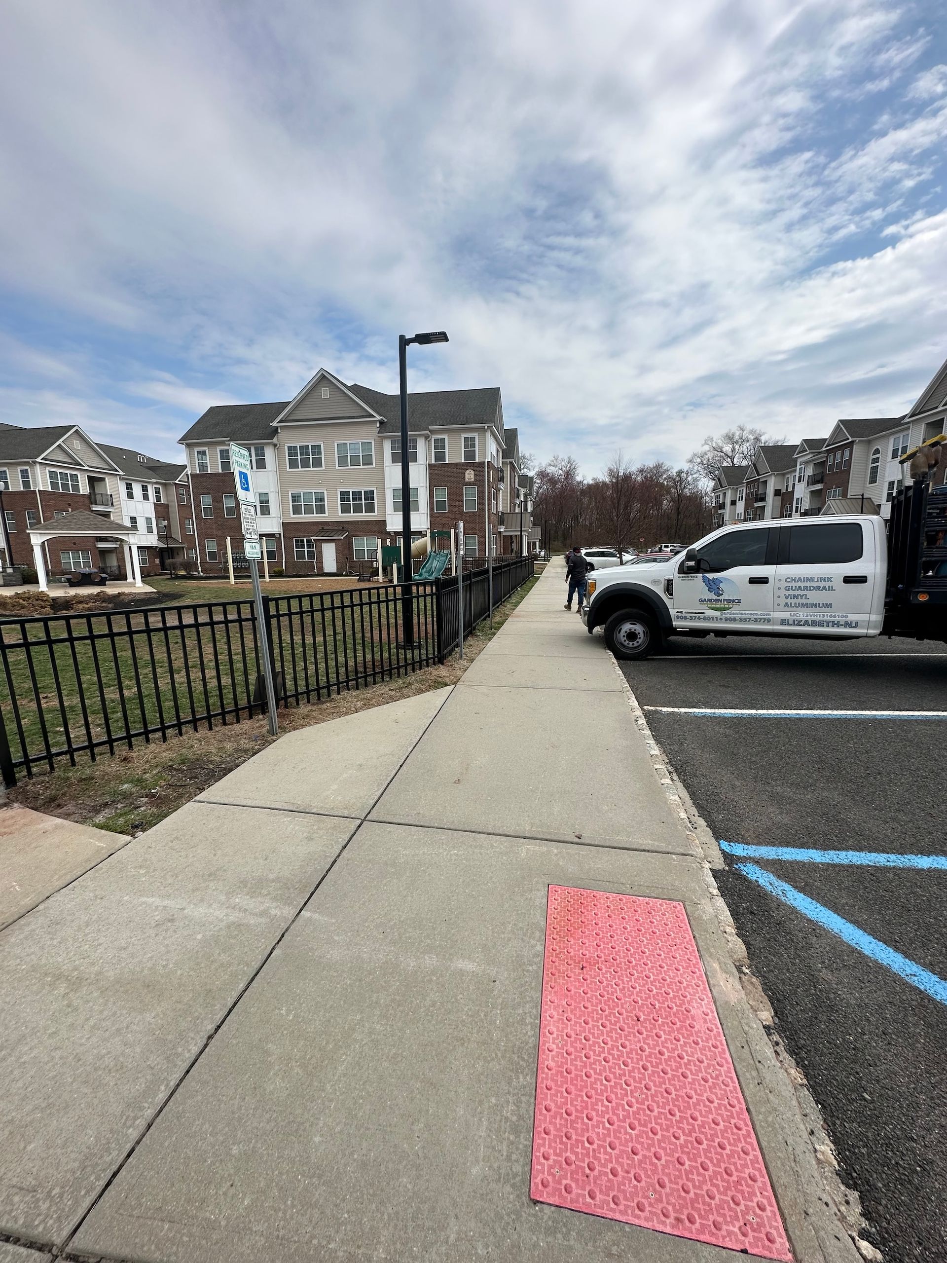Sidewalk with red tactile paving leading toward apartment buildings and a parked white truck.