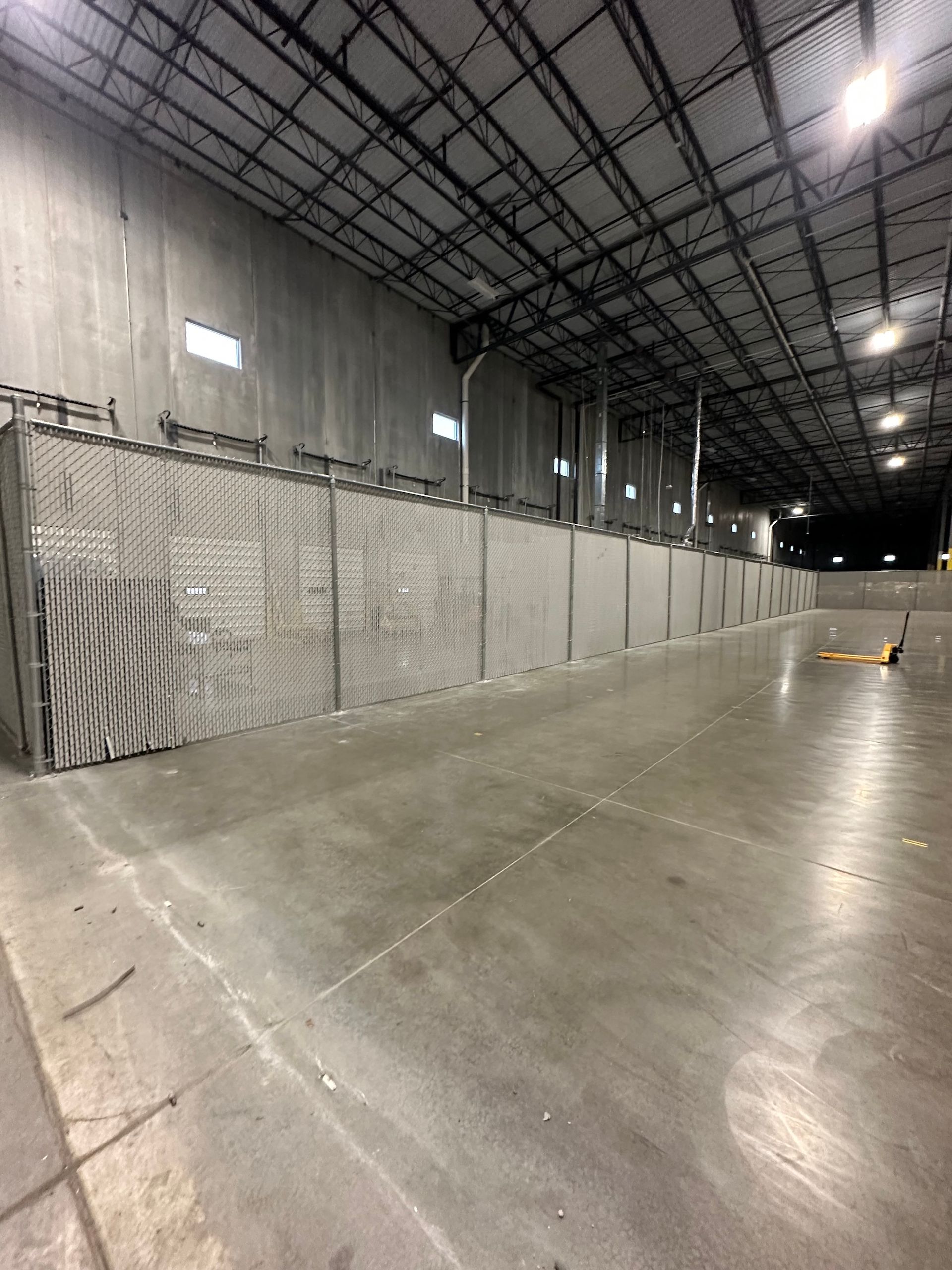 Empty industrial warehouse space with a long fence along the wall.