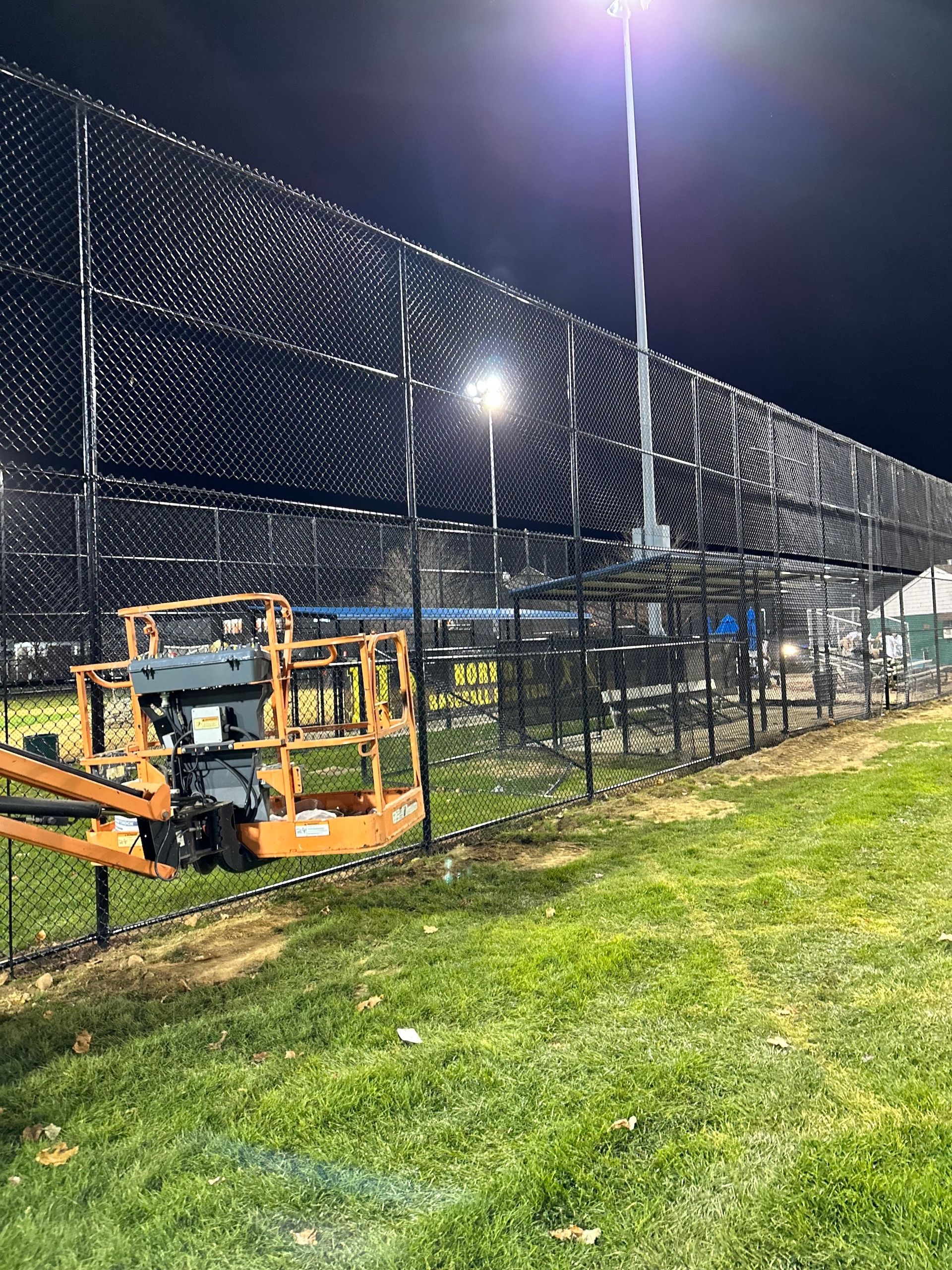 A baseball field with black netting and bright stadium lights at night. 