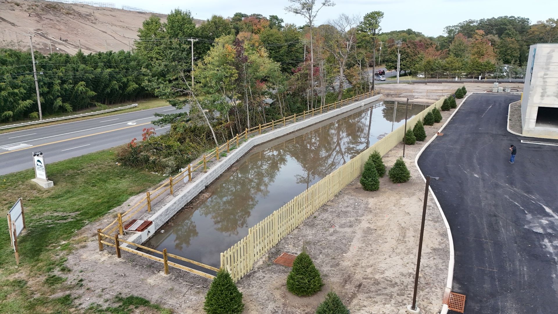 A basin with a wooden fence. The basin is filled with muddy water, surrounded by trees and a paved road.