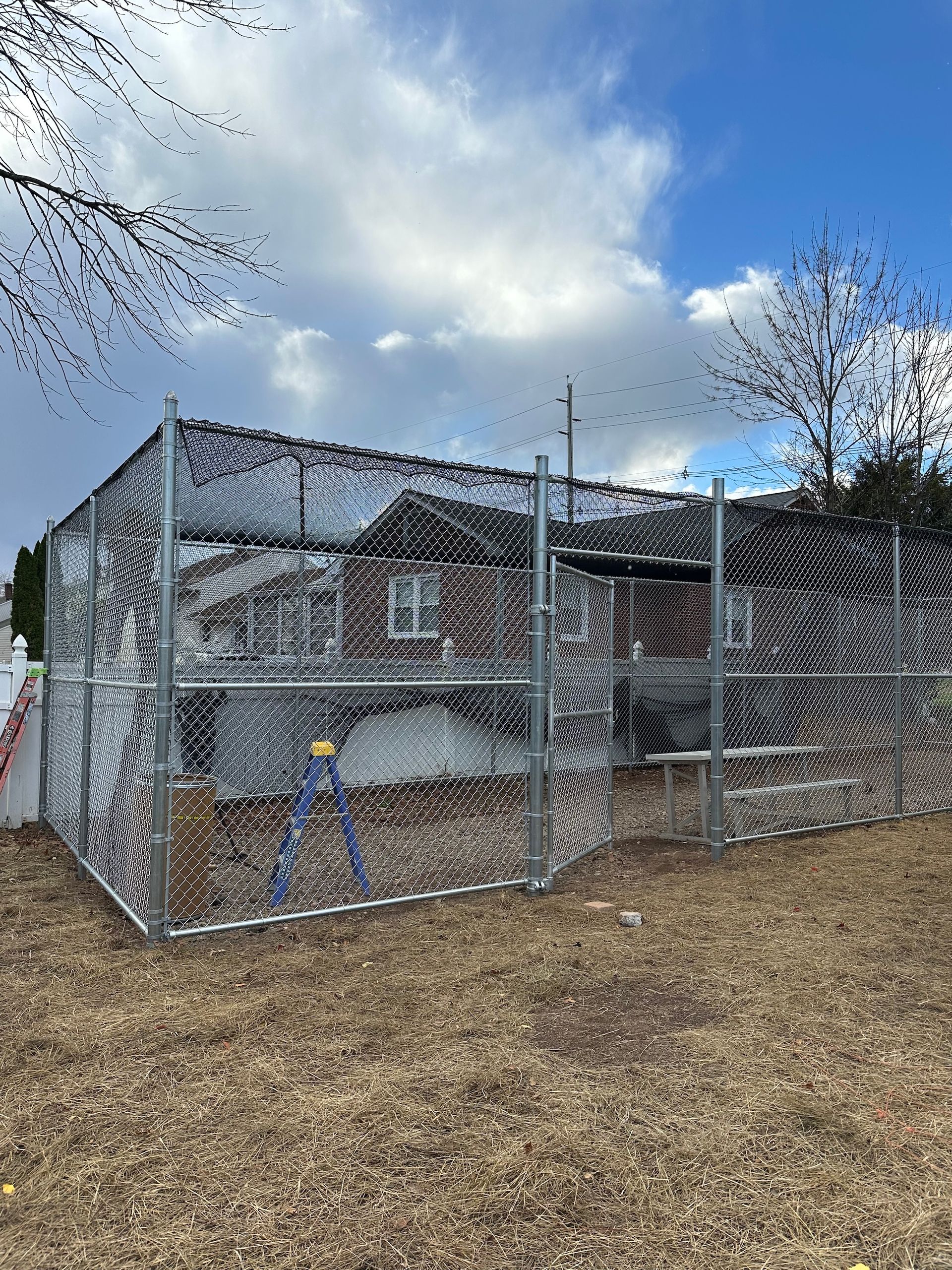 Chain-link fence enclosure around a brick building with a cloudy sky backdrop.