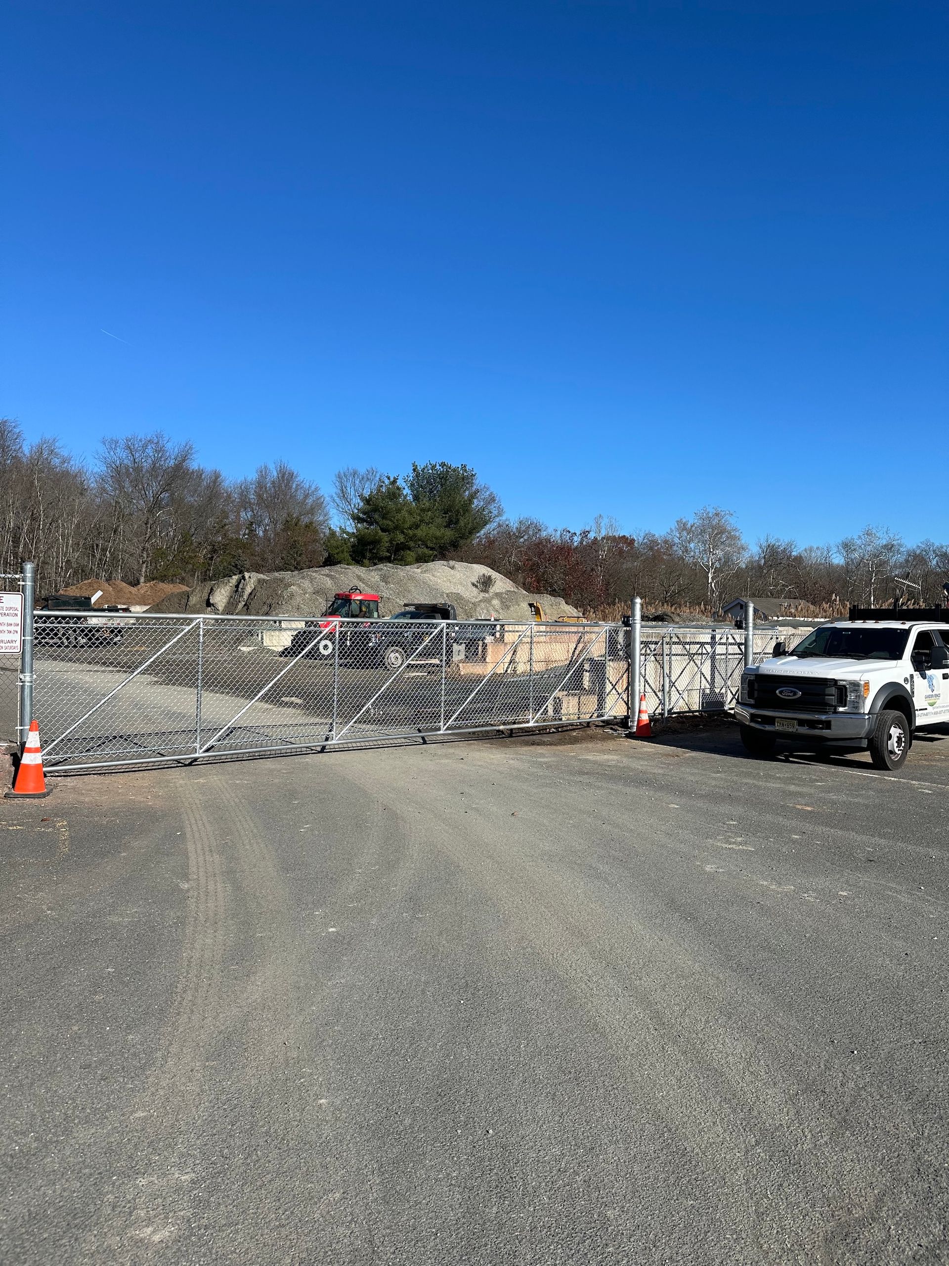 Gravel driveway blocked by metal barriers, with construction site in background, under clear blue sky.