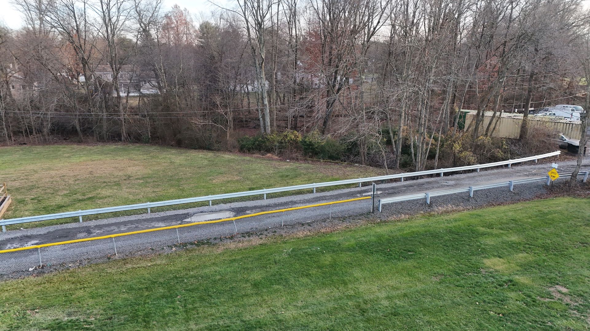 Road with yellow lines, surrounded by grass and bare trees in a rural setting.