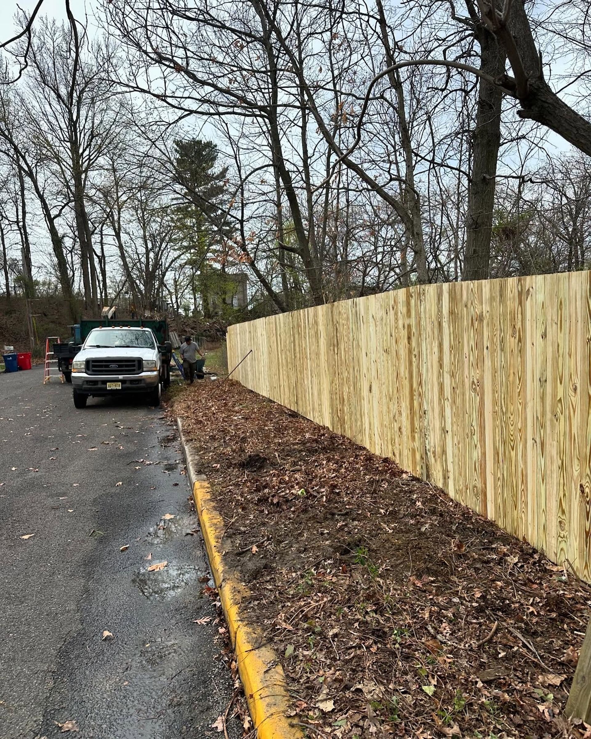 A wooden fence along a parking area, with a truck on the left and trees in the background.