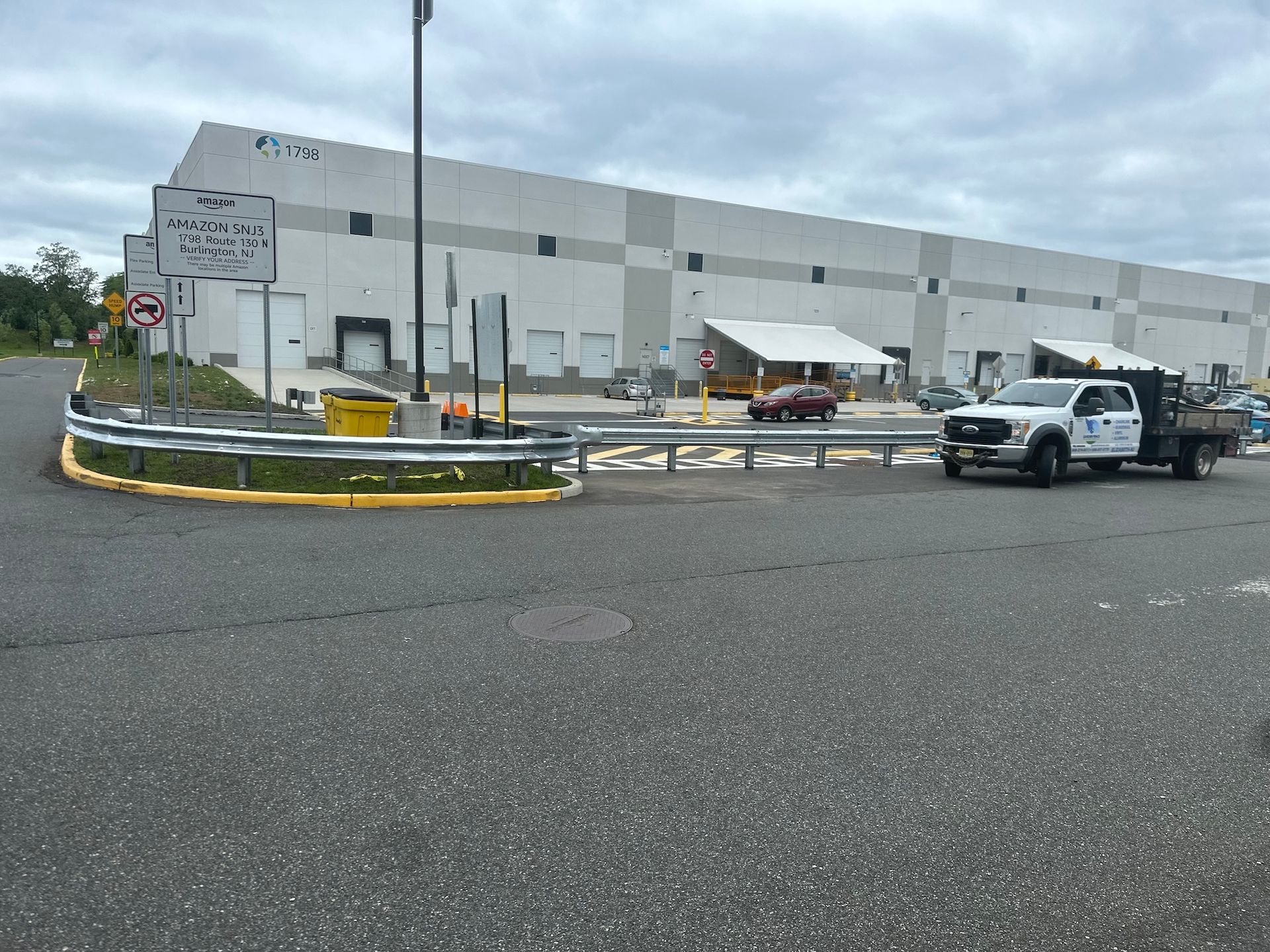 Warehouse exterior with a white truck, a guardrail, and traffic signs on an overcast day.