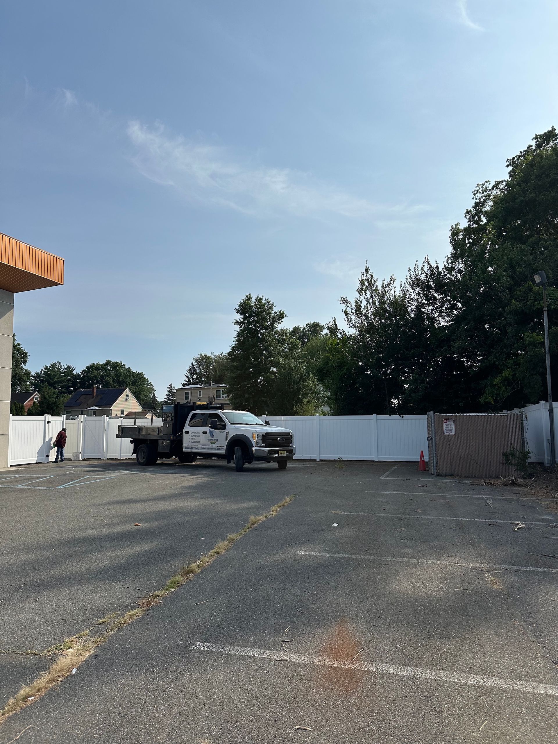 A truck parked in a gravel lot with a white fence and a partially constructed building under a blue sky.