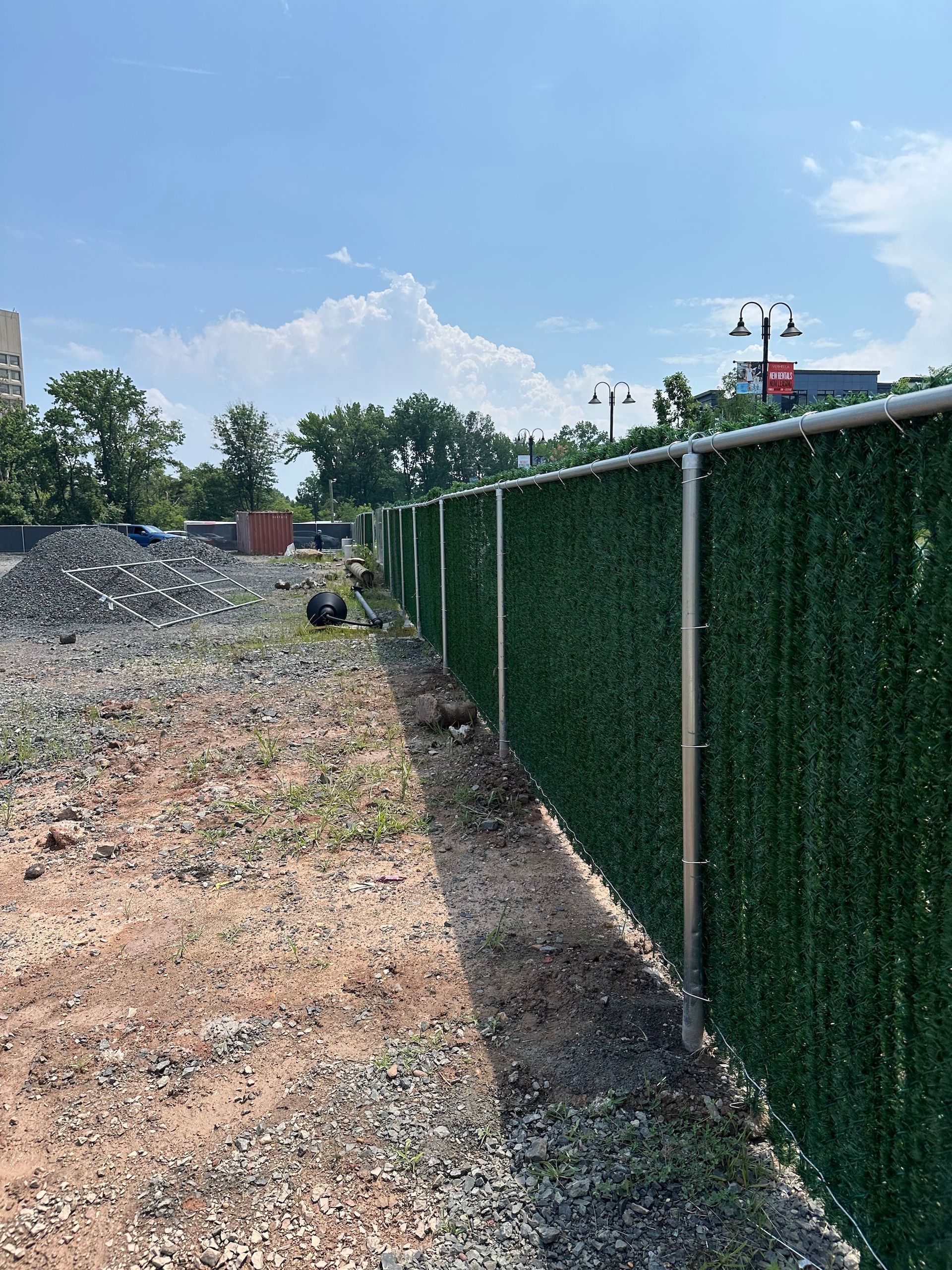 A construction site bordered by a green privacy fence on a sunny day.