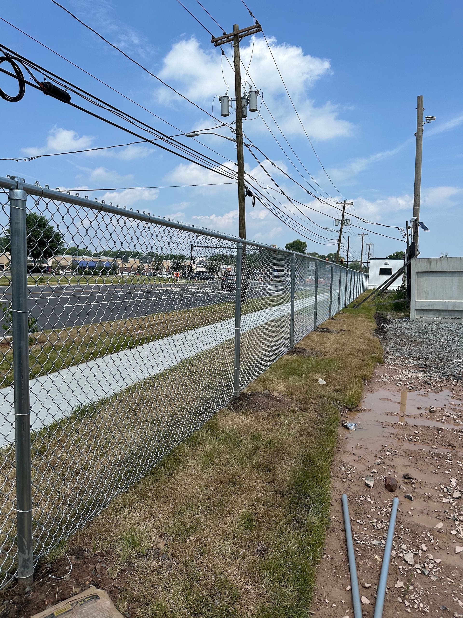 A long fence covered in green plastic leaves lines a construction site.