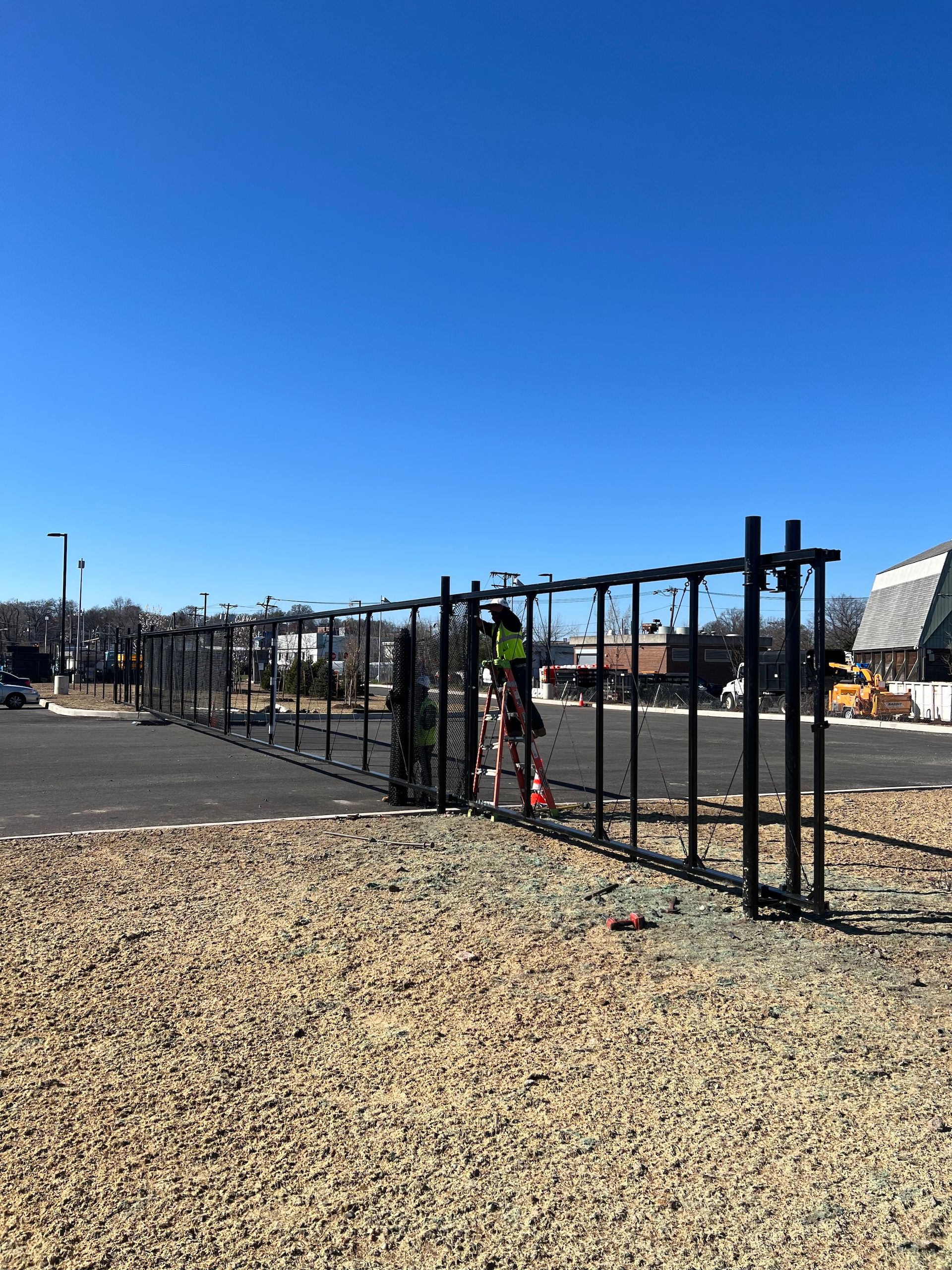 Black metal fence being installed in a gravel area on a sunny day.