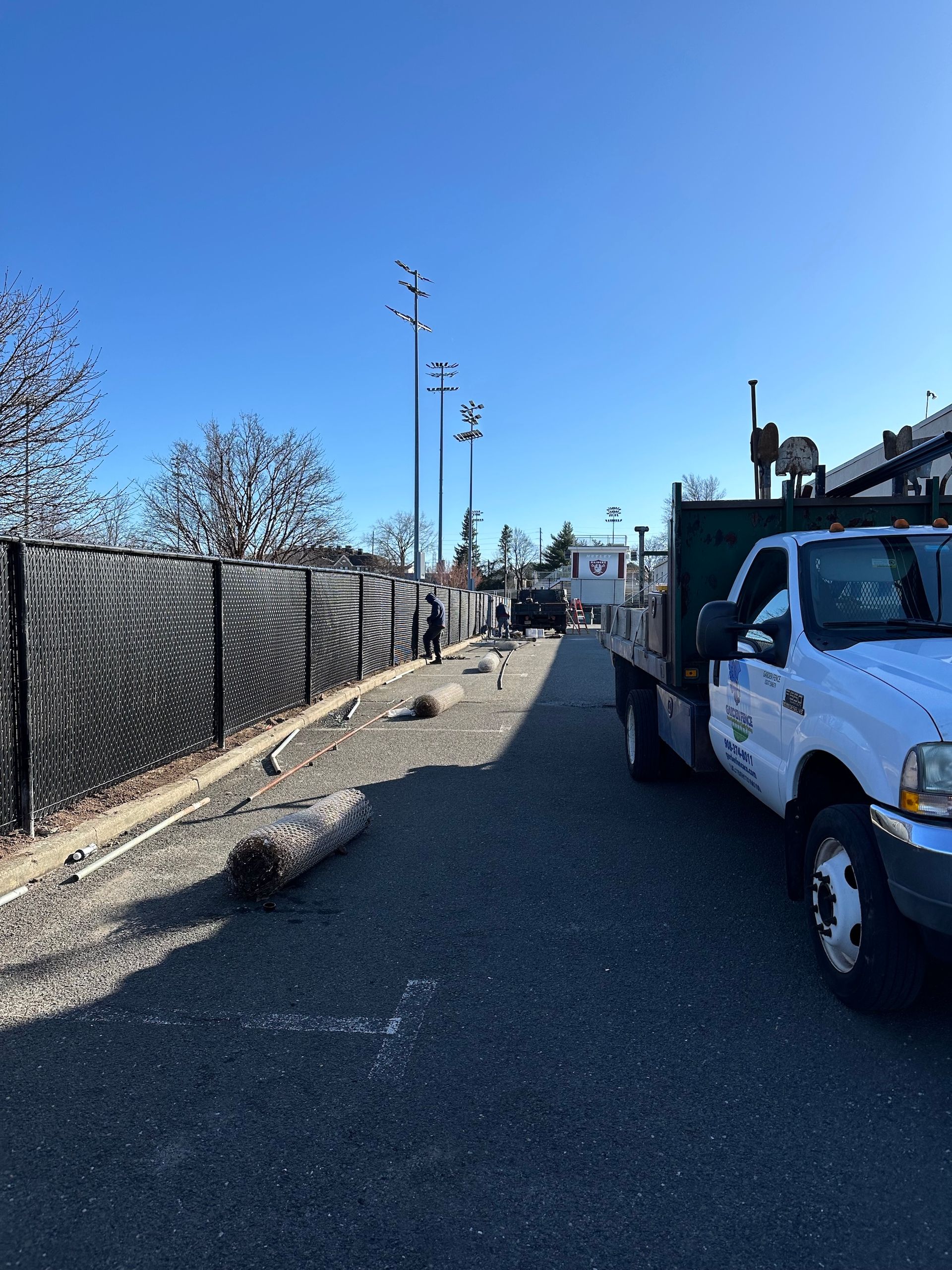 A gravel path with a truck parked on the right. A black fence borders the path on the left.