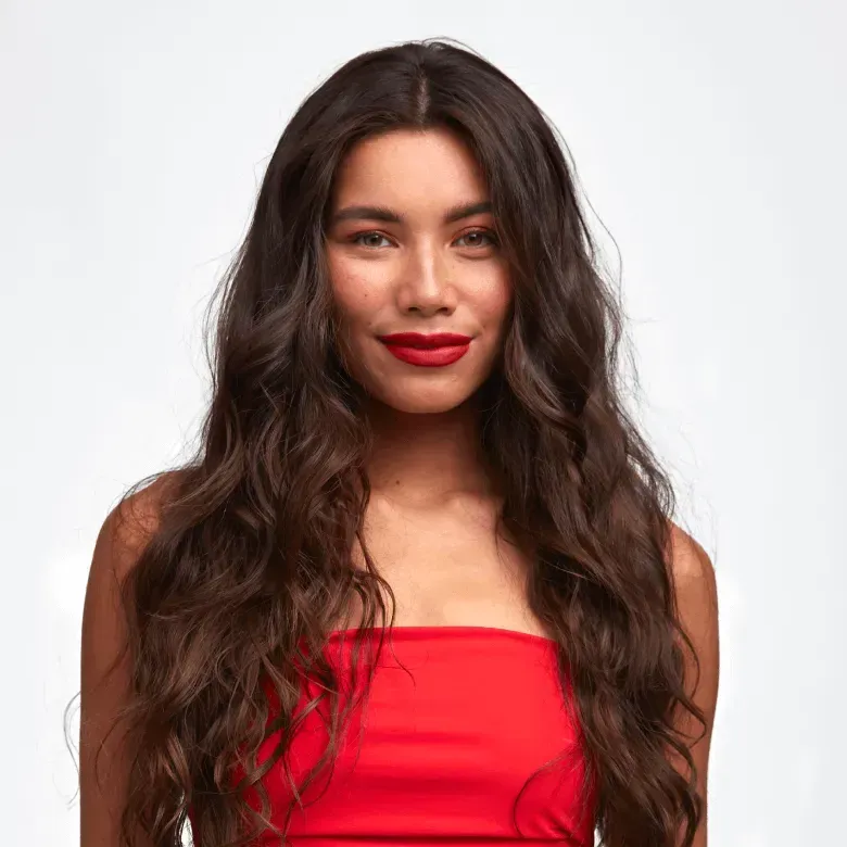 Una mujer con cabello largo y castaño lleva un top rojo y lápiz labial rojo.