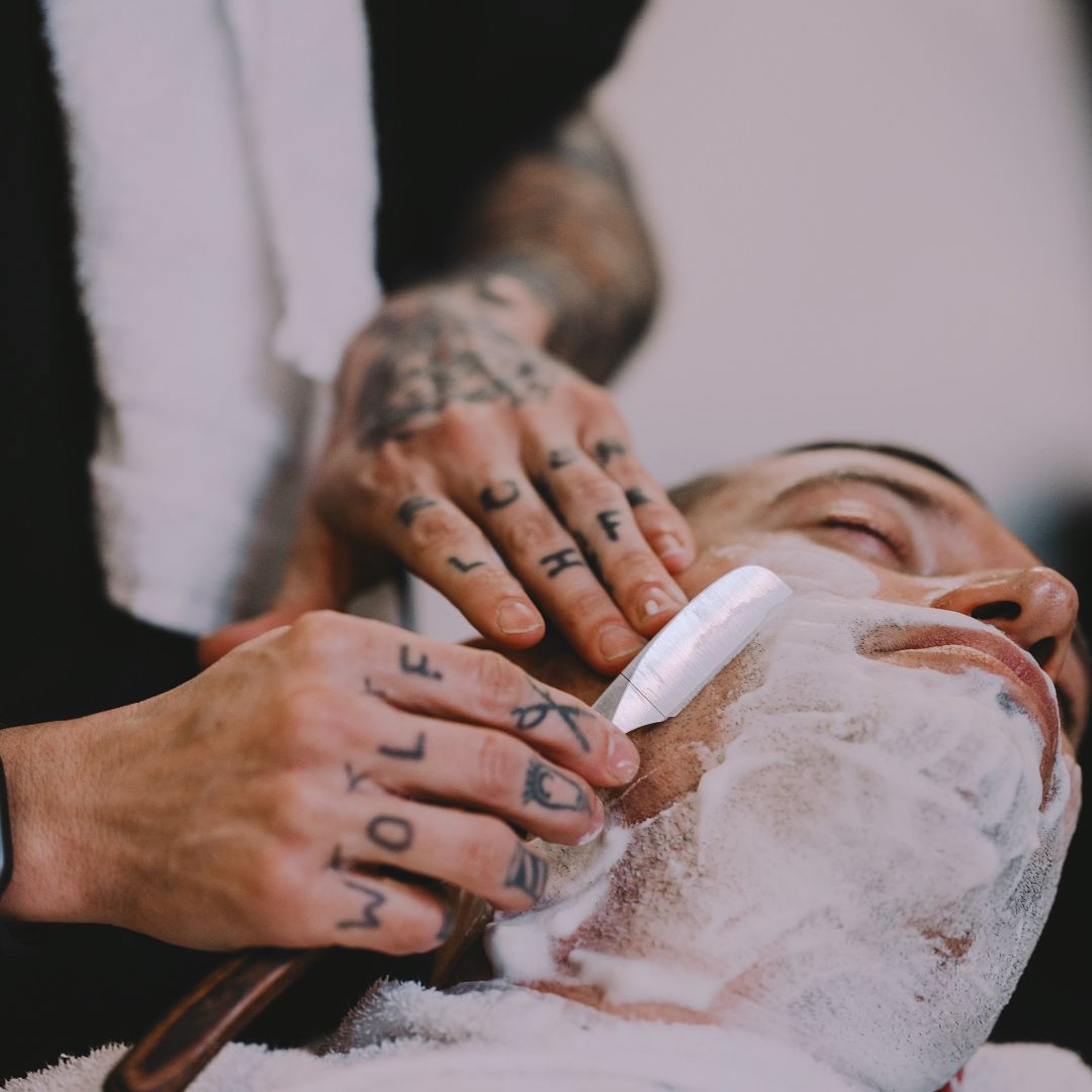 Un barbero le afeita la cara a un hombre con un lobo tatuado en las manos