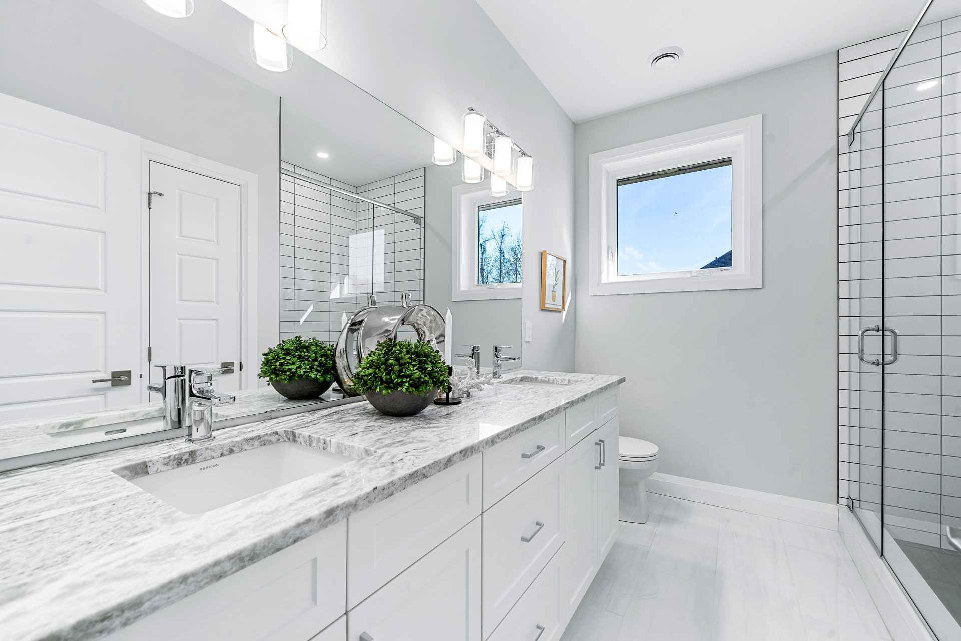 A bathroom with two sinks , a toilet , and a large mirror Fidelity Homes Signature build in Brighton Township
