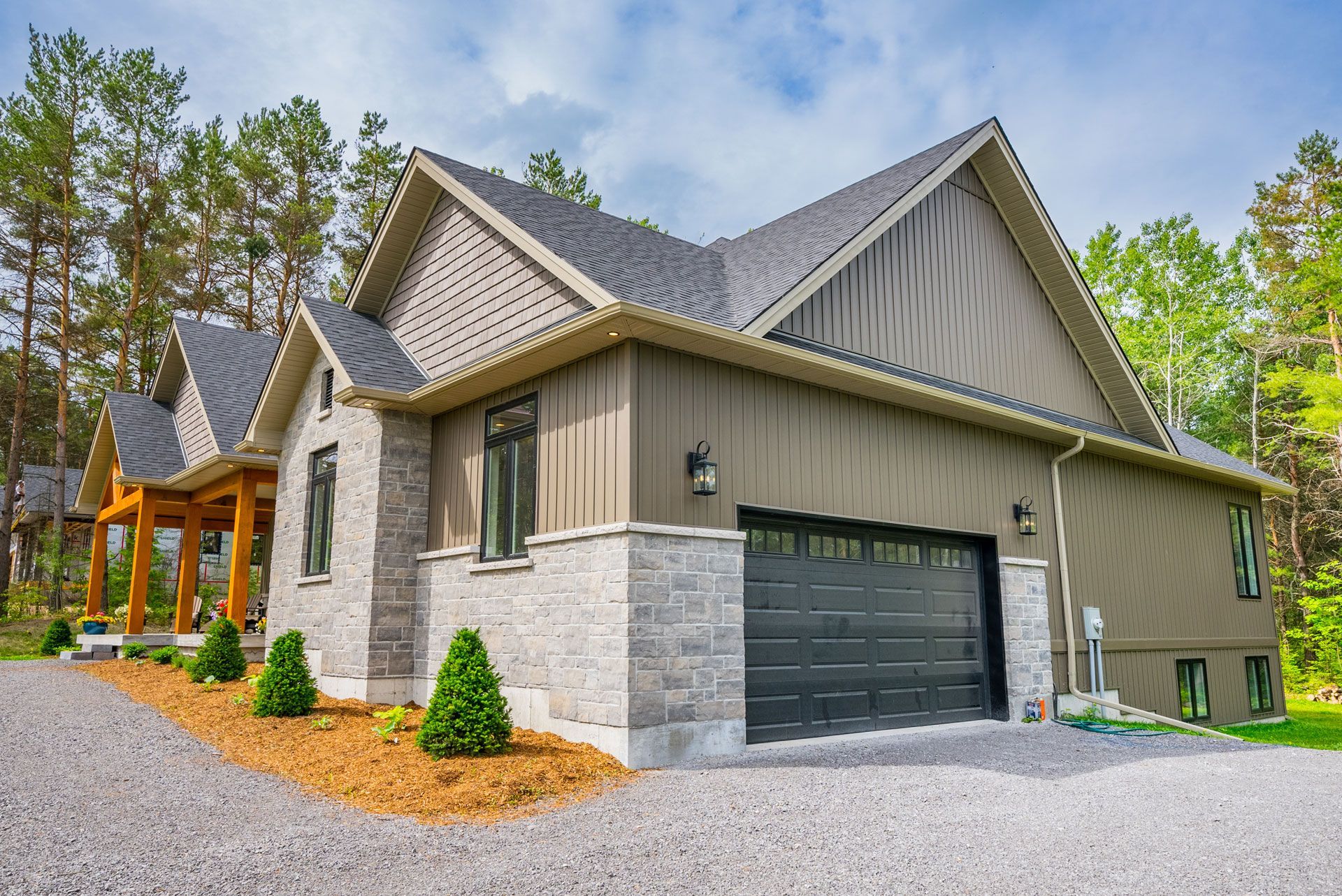 A large house with a black garage door is surrounded by trees by Fidelity Homes in Castleton Ontario