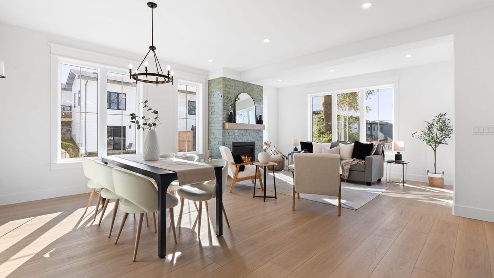 Bright open dining and living room with white walls, wood floors, and large windows.