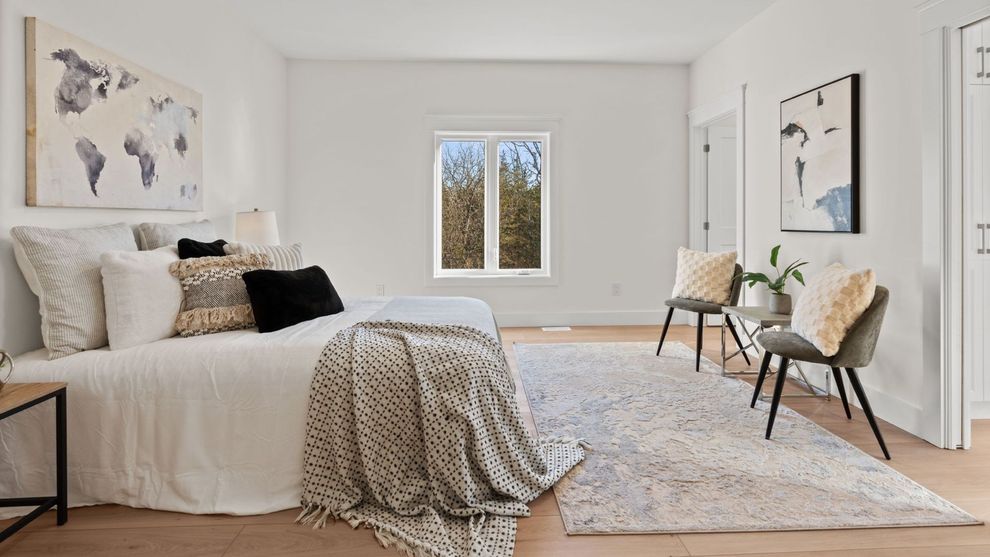 Bright minimalist bedroom with a bed, rug, chairs, and wall art beside a small window