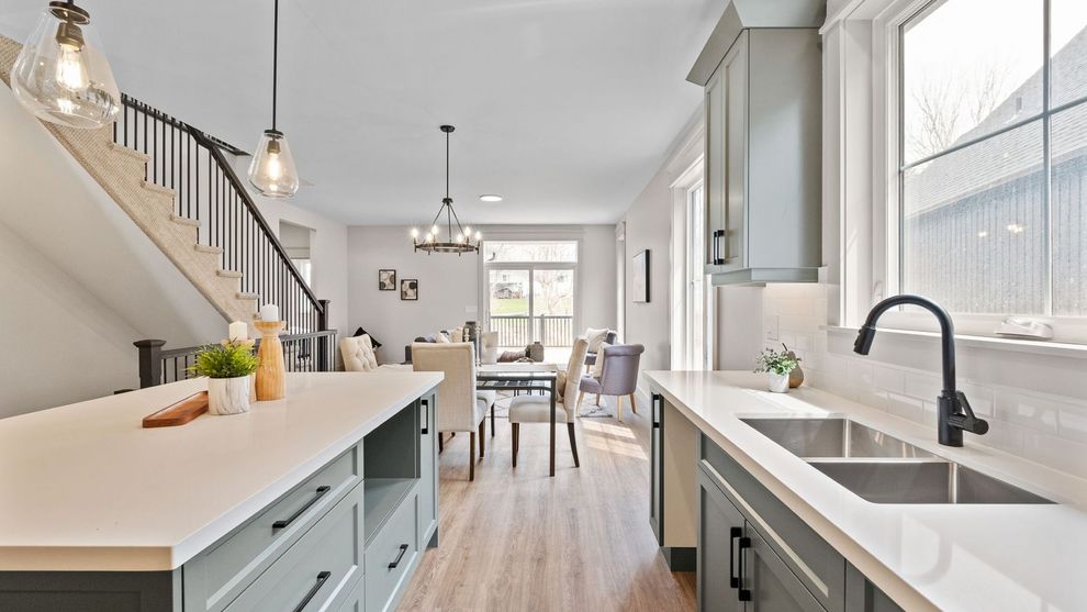Bright modern kitchen with white island, farmhouse sink, staircase, and dining area in the background