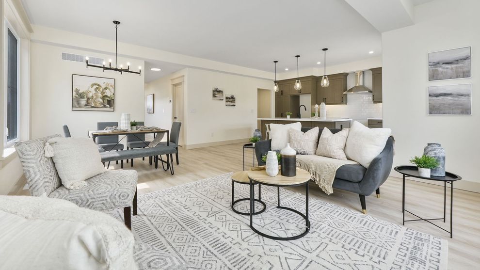 Bright modern living room with gray sofa, patterned rug, dining table, and open kitchen.