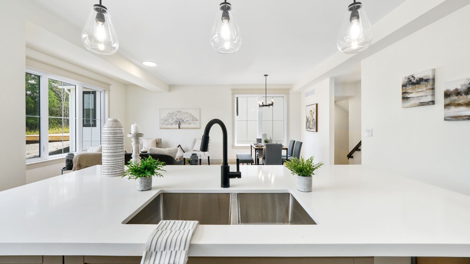 Bright white modern kitchen with large island, black faucet, pendant lights, and garden view
