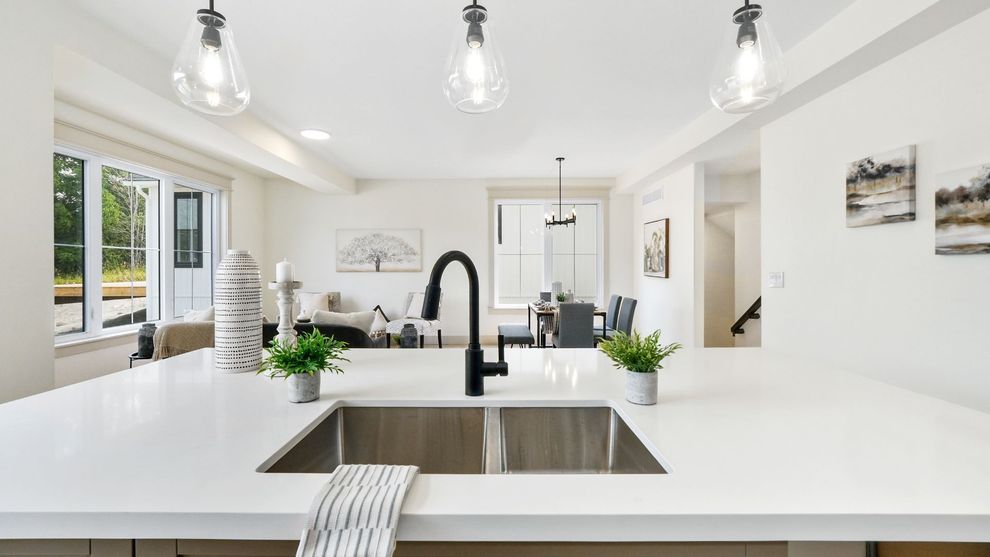 Bright white modern kitchen with large island, black faucet, pendant lights, and garden view