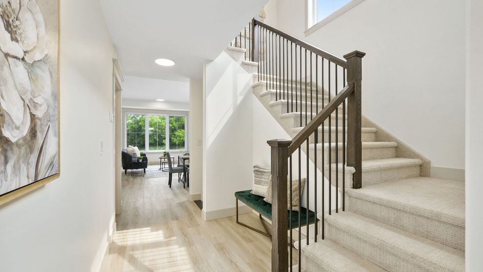 Bright hallway with staircase, white walls, wood floors, and a view to a dining area and patio doors.