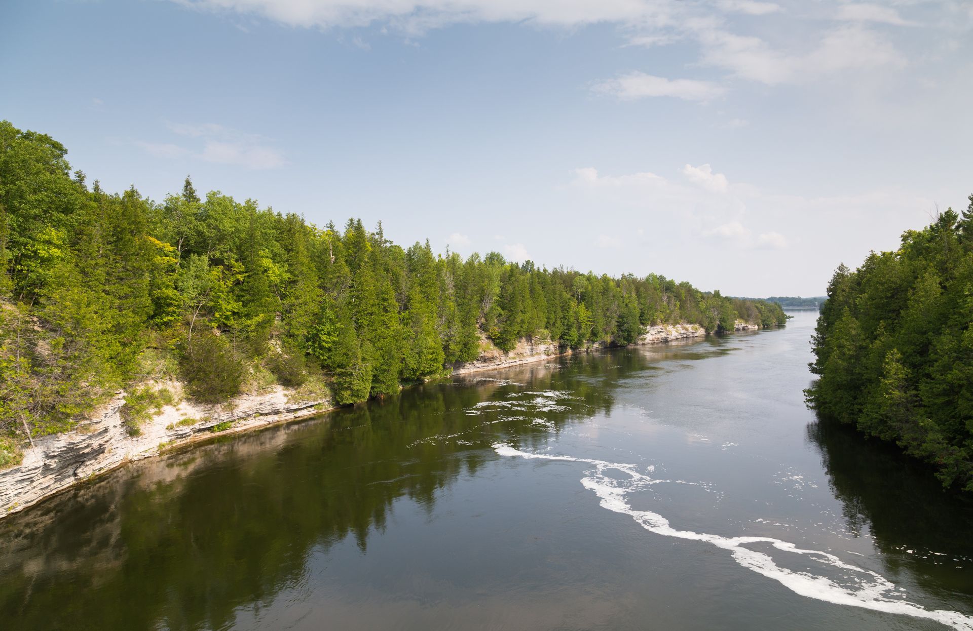 A view of the Trent River surrounded by trees and rocks on a sunny day