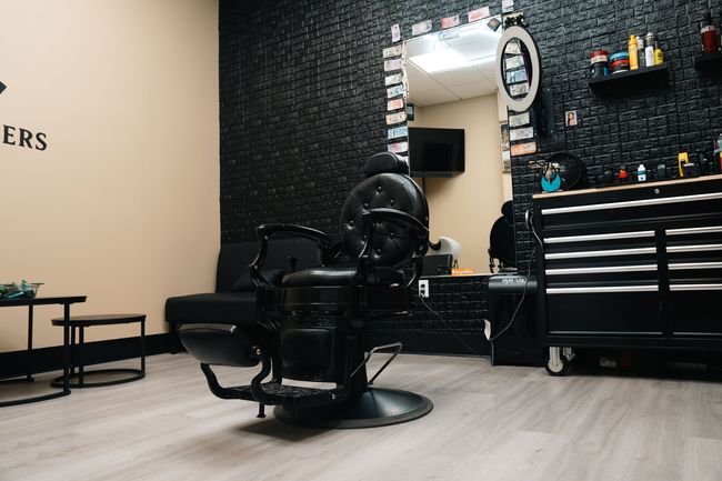 Modern barbershop interior with black barber chair, mirror, styling tools, and checkered wall.