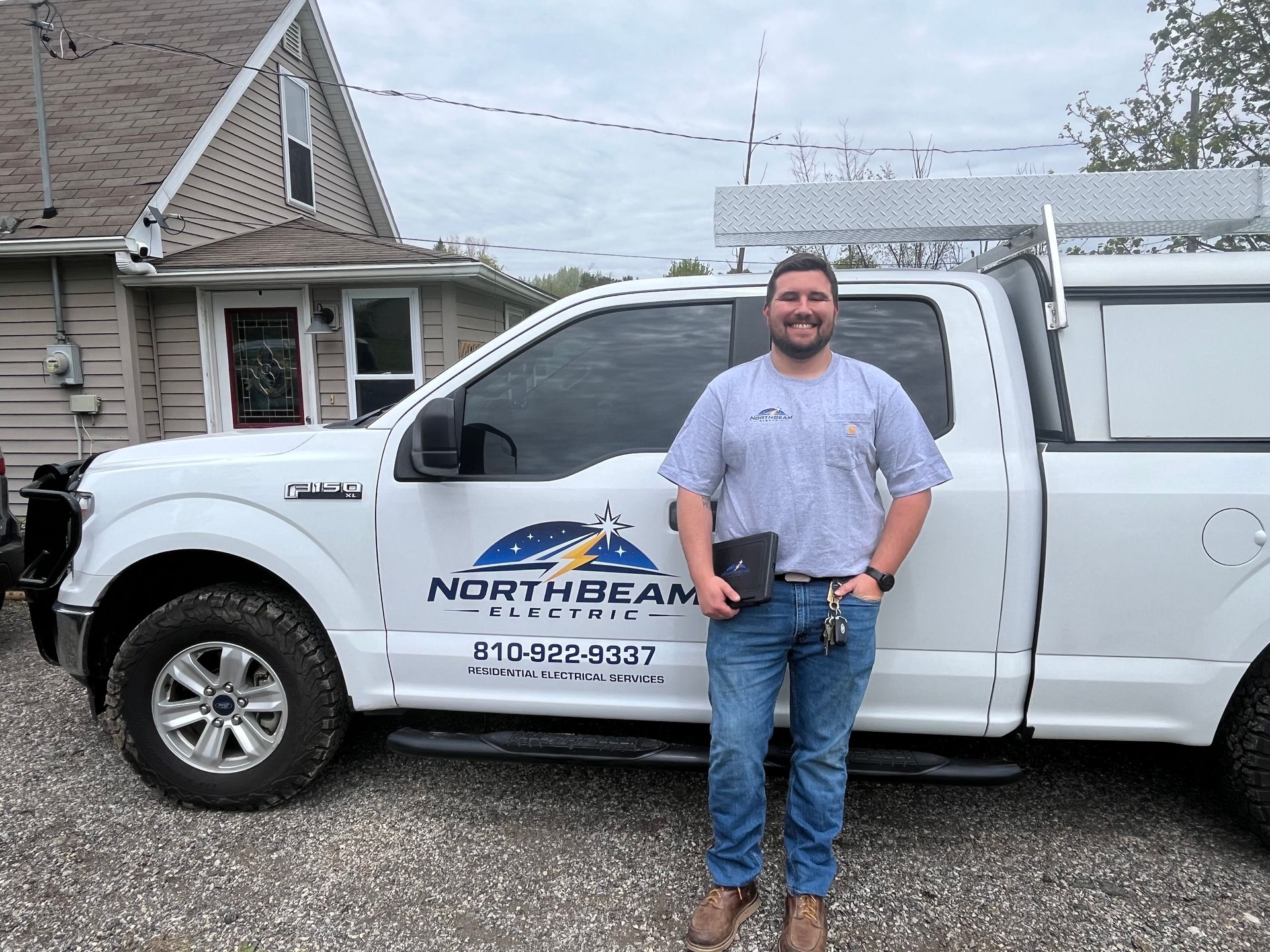 Man standing beside a white Northbeam service truck in a driveway, holding keys and smiling.
