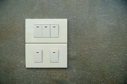 White light switch panel on a gray wall with three toggles and two switches