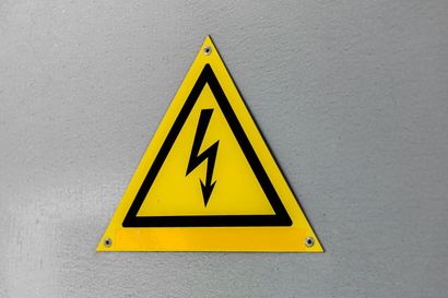 Yellow high-voltage warning sign with black lightning bolt on a gray wall