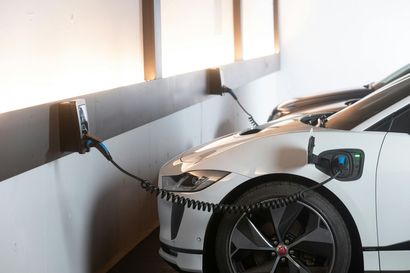 White electric car charging indoors from wall-mounted stations, connected by cables.