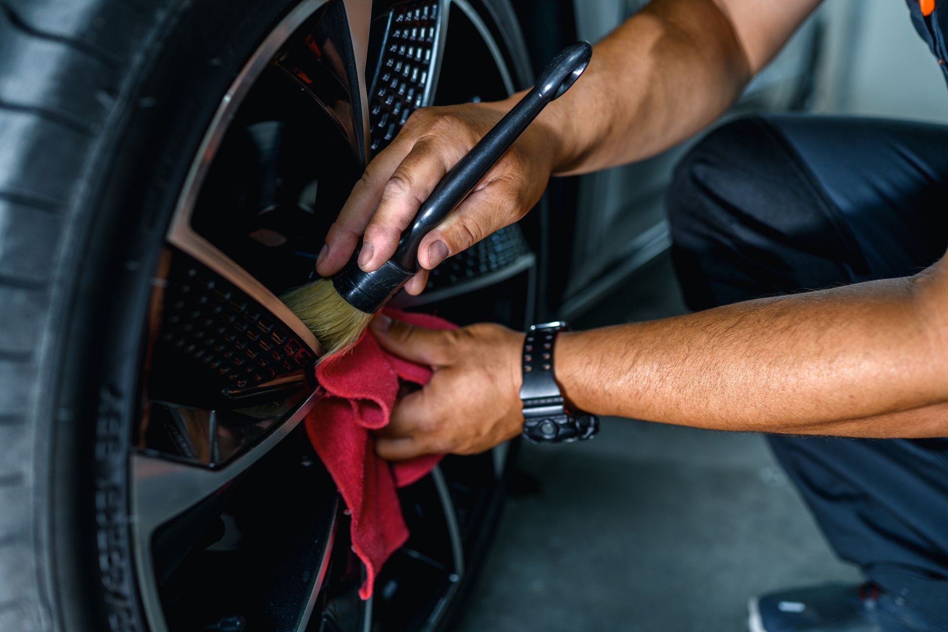 A man is cleaning a car wheel with a brush and towel.