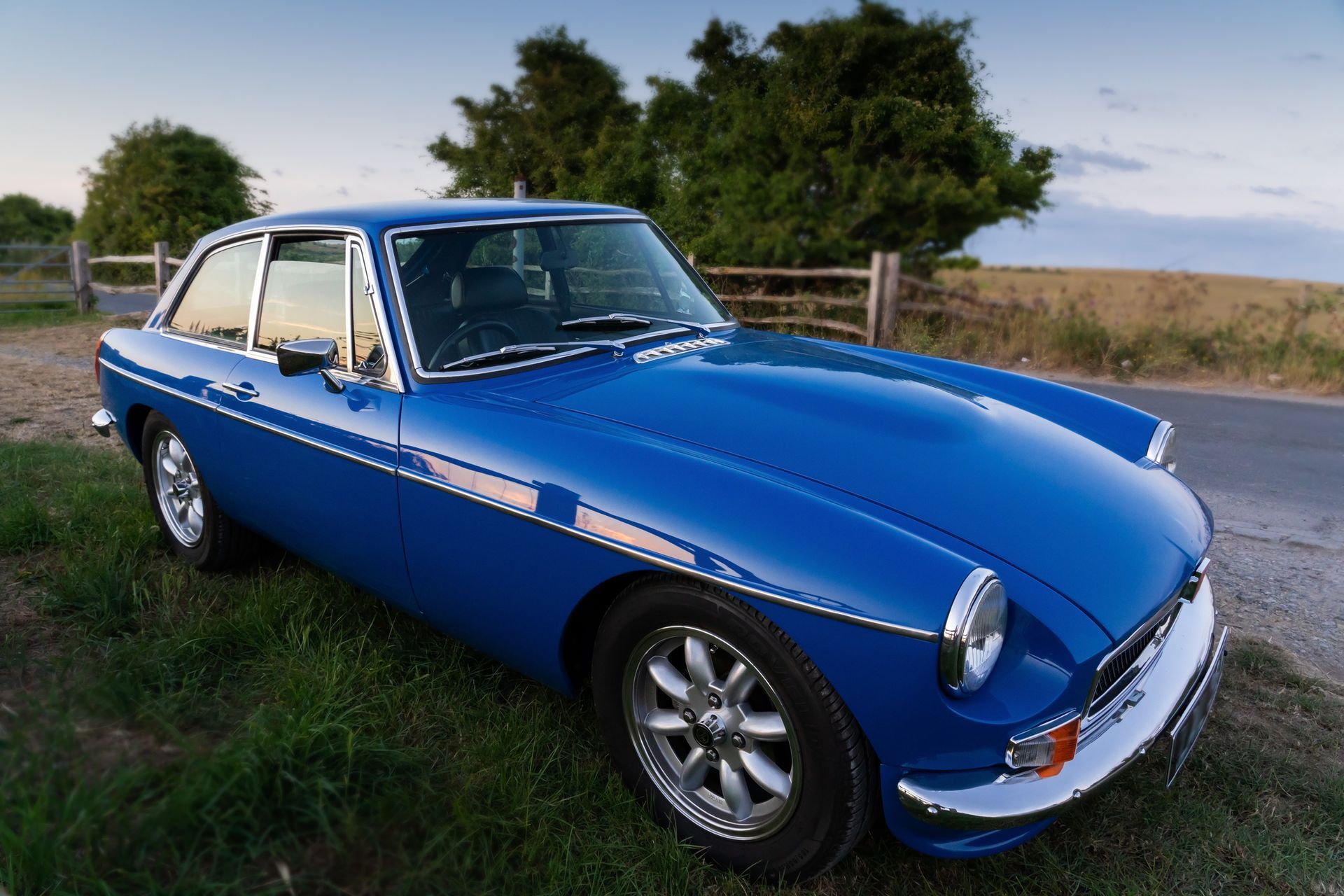 A blue car is parked in the grass on the side of the road.