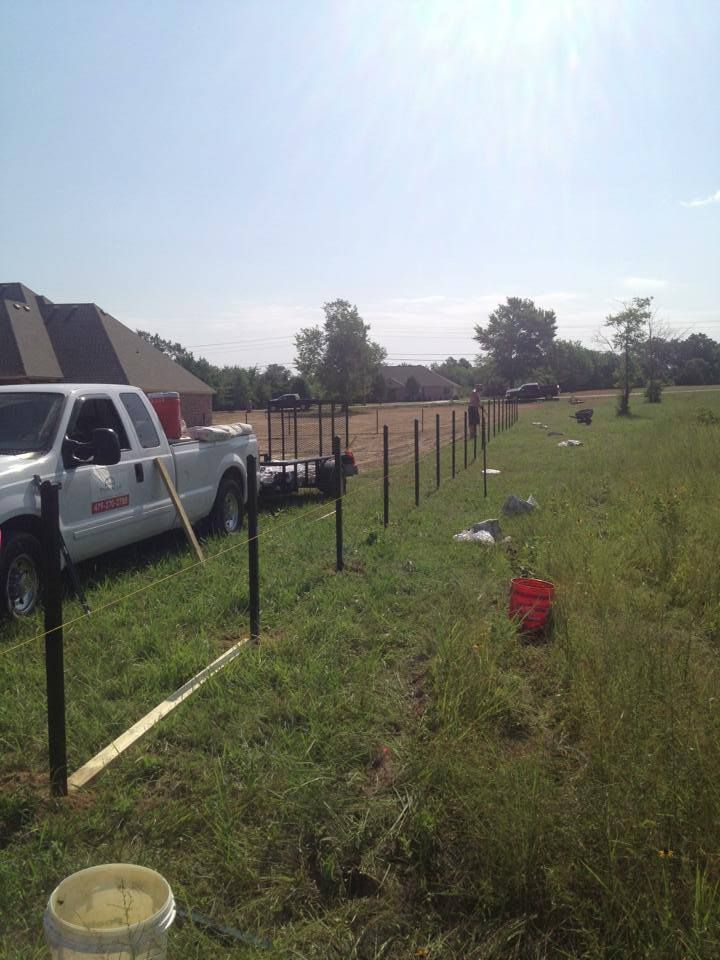 A white truck is parked in a grassy field next to a fence.