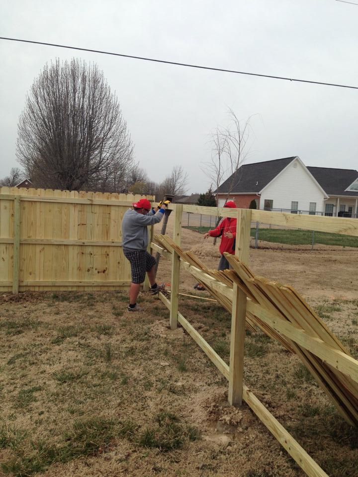 Two men are working on a wooden fence in a yard.