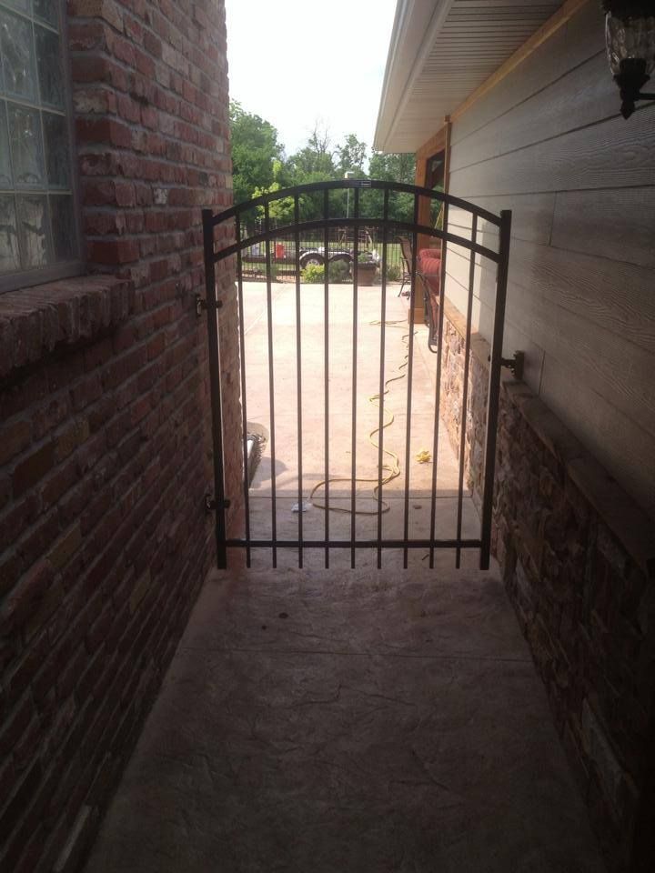 A metal gate is between a brick building and a driveway.