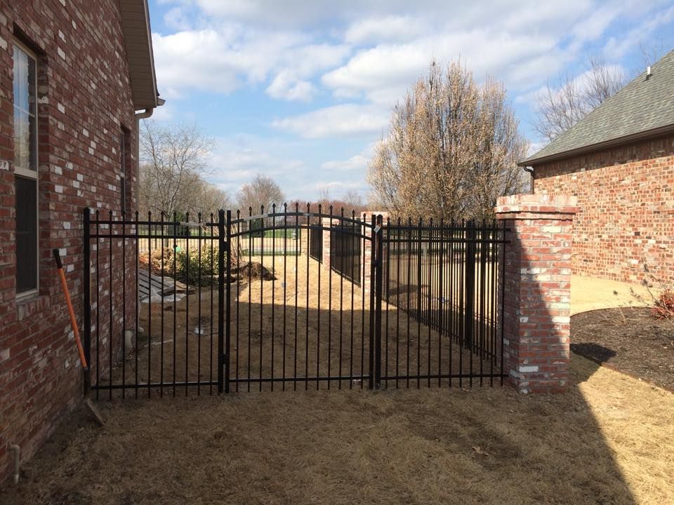 A black wrought iron gate is in the backyard of a brick house.