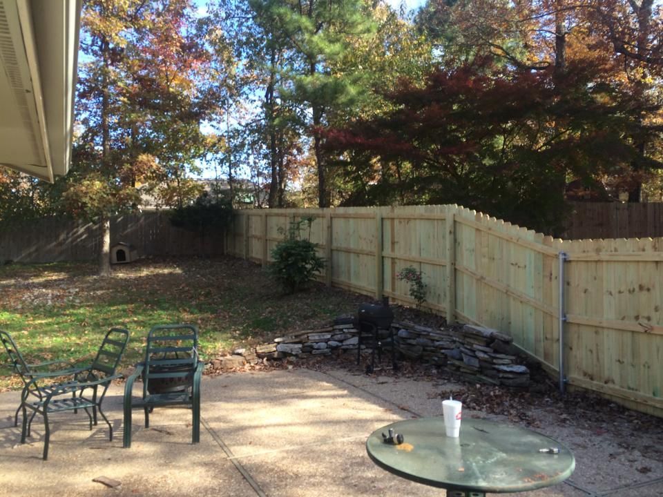 A wooden fence surrounds a patio with chairs and a table.