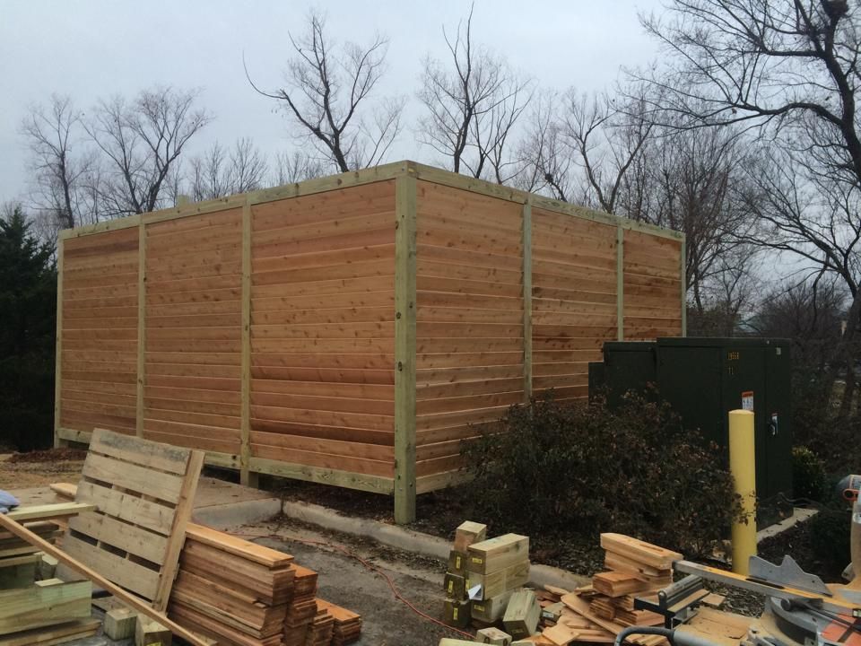 A wooden fence is being built in a yard with trees in the background